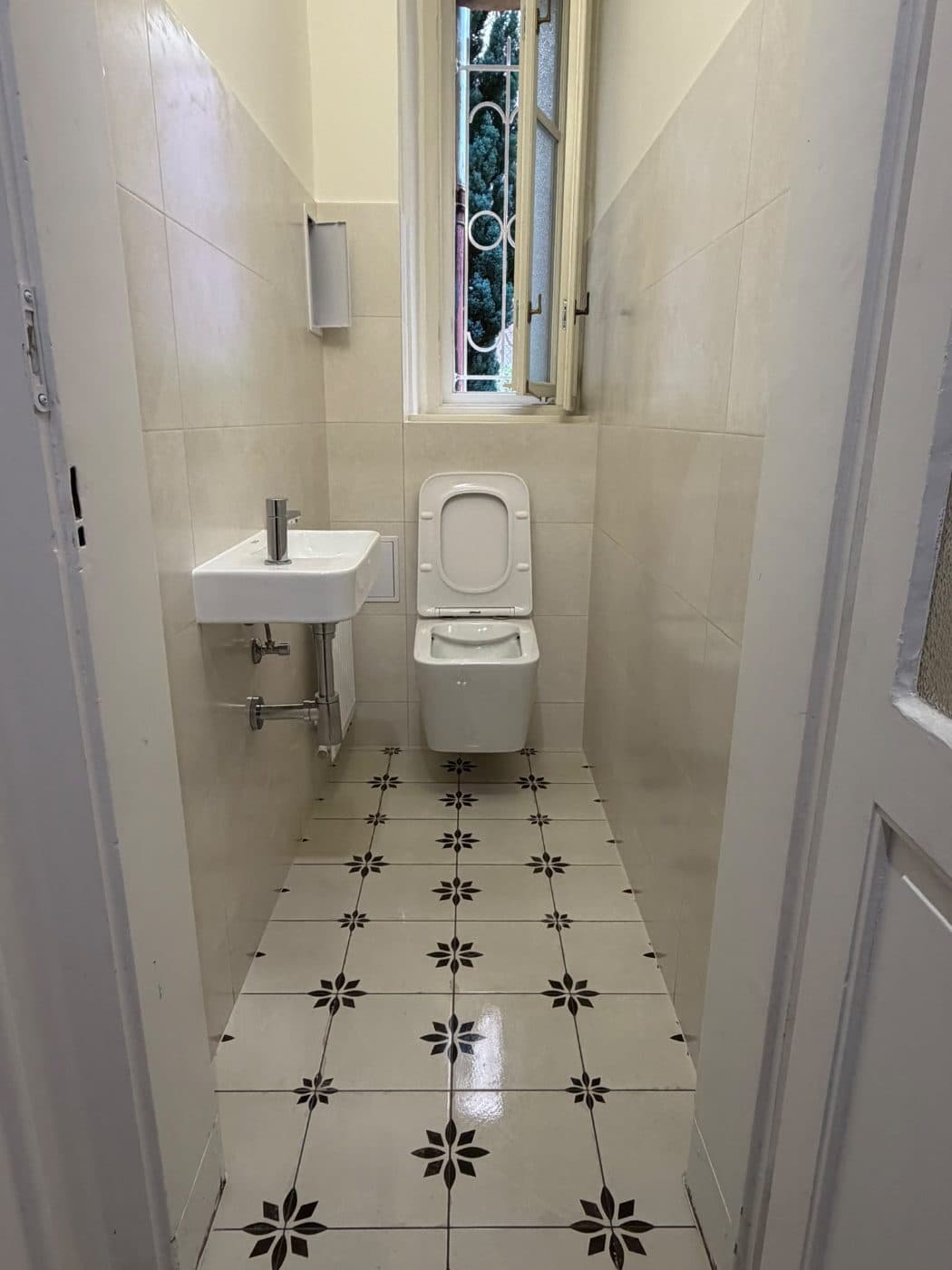Hotové WC se závěsnou mísou, malým umývátkem a dlažbou s černým ornamentem