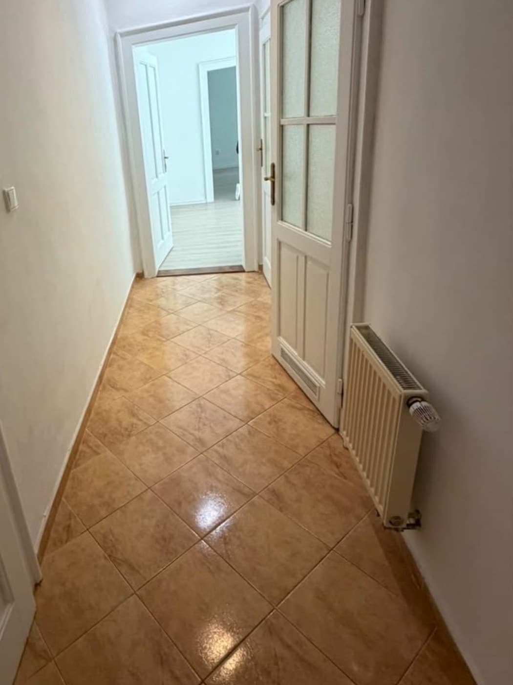 Původní chodba od vstupu s oranžovou dlažbou kladenou na koso, vpravo prosklené dveře a radiátor