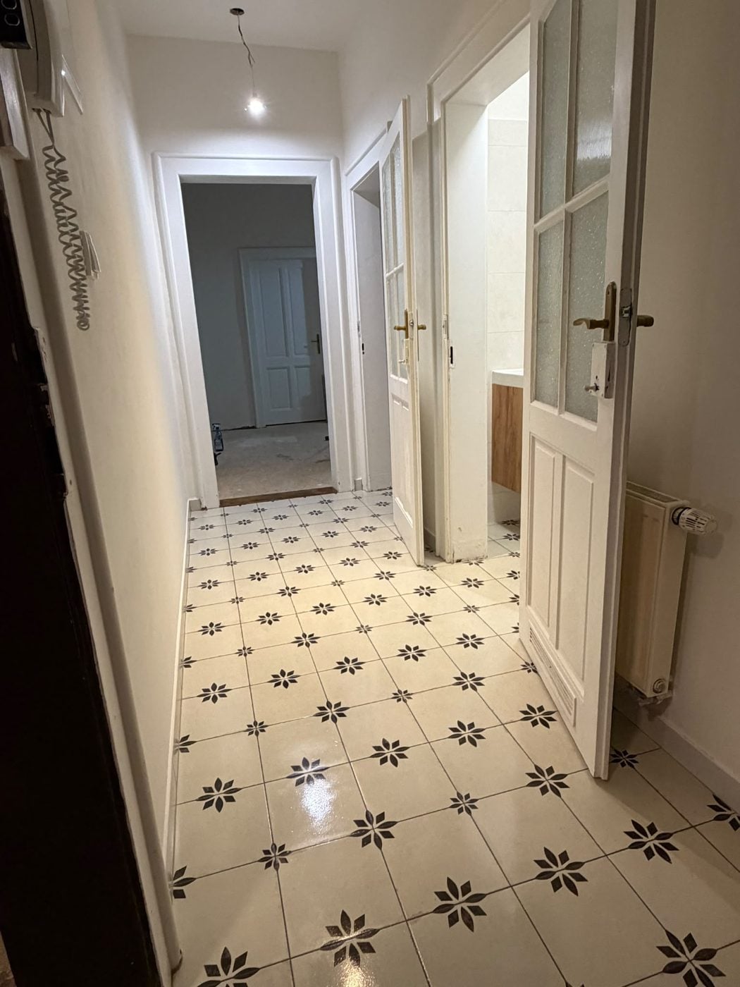 Hotová chodba s bílými stěnami, ornamentální dlažbou a prosklenými dveřmi do koupelny