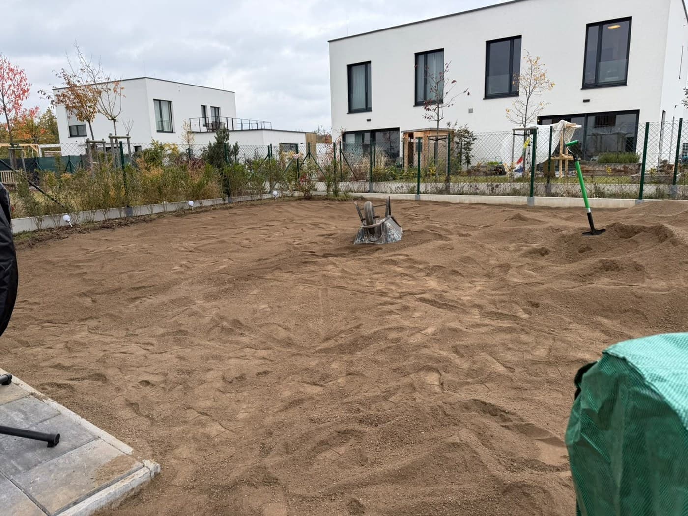 Rozhrnutá a srovnaná zemina na celé ploše zahrady, za plotem bílé novostavby