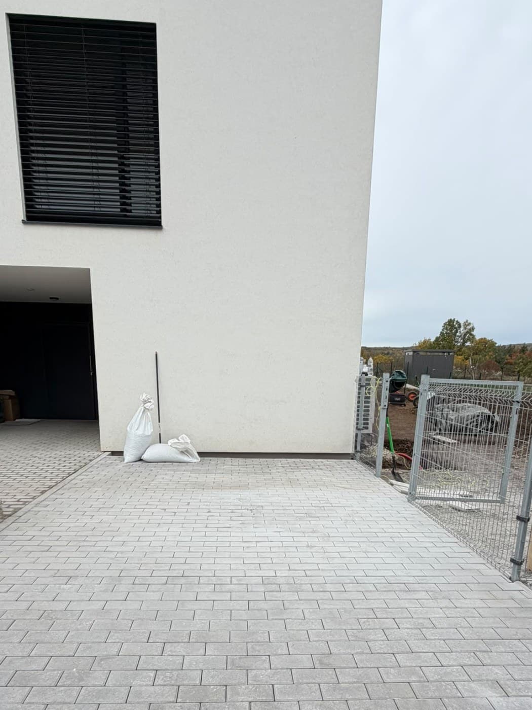 Hotová plocha ze šedé zámkové dlažby před vstupem do domu, vpravo branka v plotě