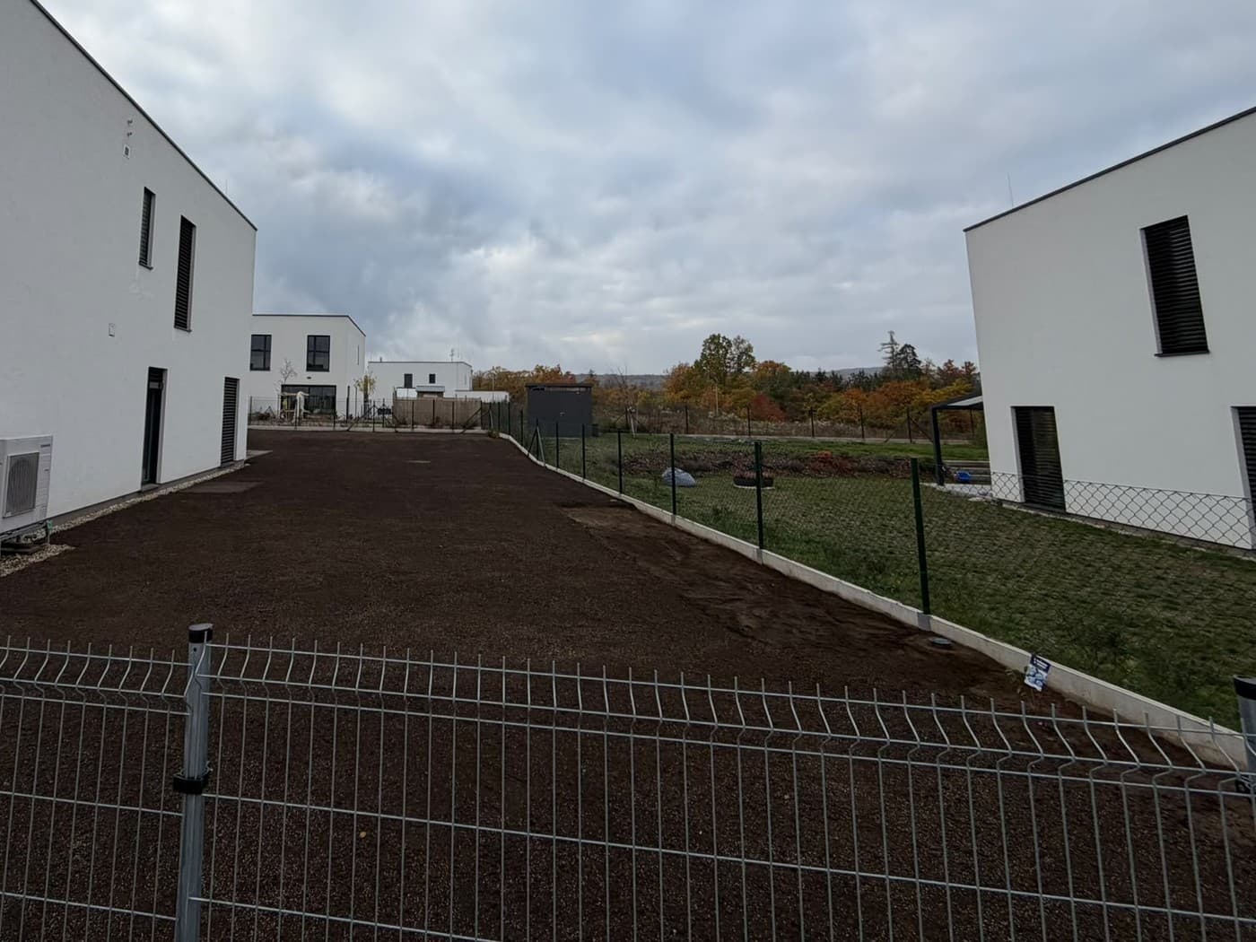 Hotový srovnaný a uhrabaný terén podél domu, tmavá zemina až k plotu sousední zahrady